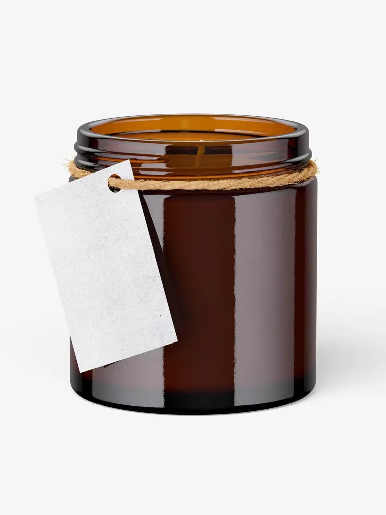 A tall amber glass candle jar with a blank hanging paper tag tied around its neck.