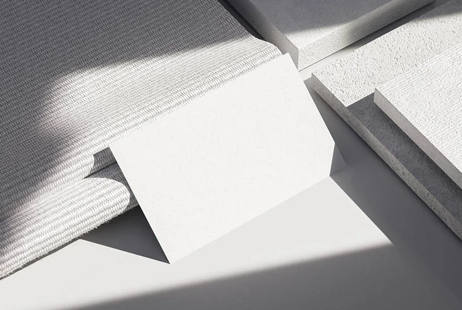 Blank white business card angled across a gray surface beside folded textured fabric and layered pale stone slabs.