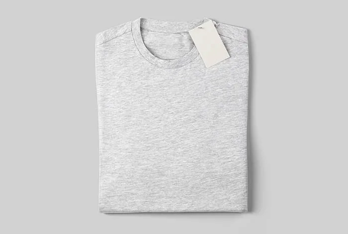 Top view of a folded light gray heather T-shirt with a blank white tag near the collar on a pale gray background.