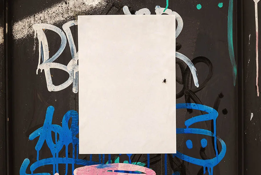 Blank off-white poster centered on a dark wall covered with colorful graffiti.