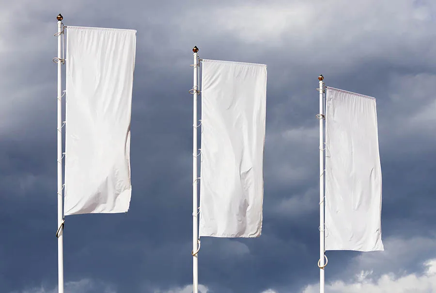 Three blank white fabric flags on slender poles against a cloudy blue-gray sky.